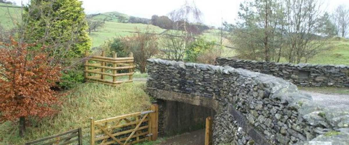 A stone bridge over a small stream, surrounded by grassy fields and trees.