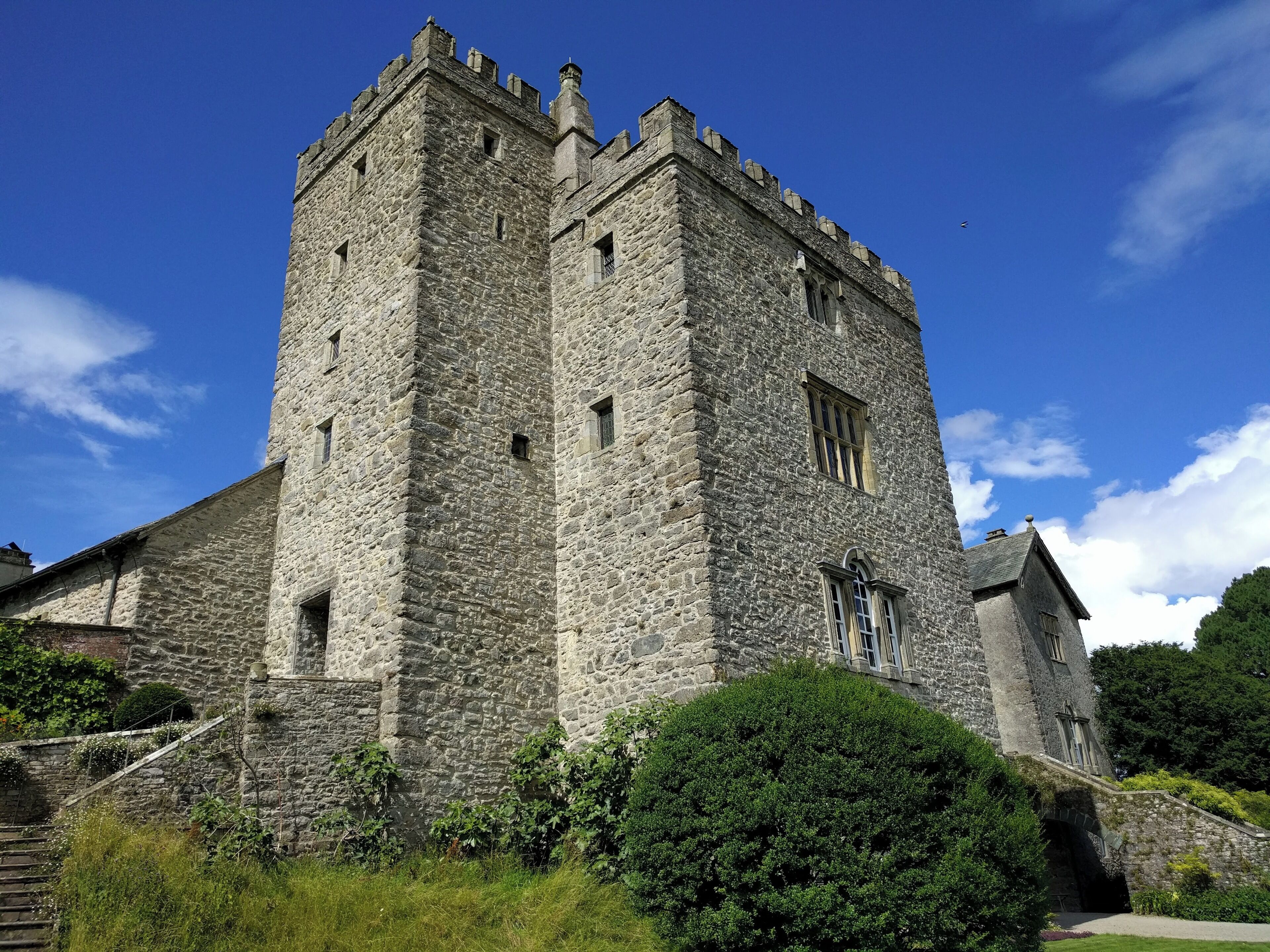 A large stone castle with a tall tower, surrounded by greenery and a clear blue sky.