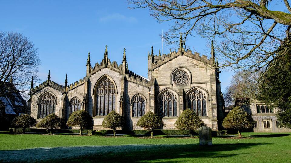 A historic church with Gothic architecture, surrounded by a well-maintained lawn and mature trees.