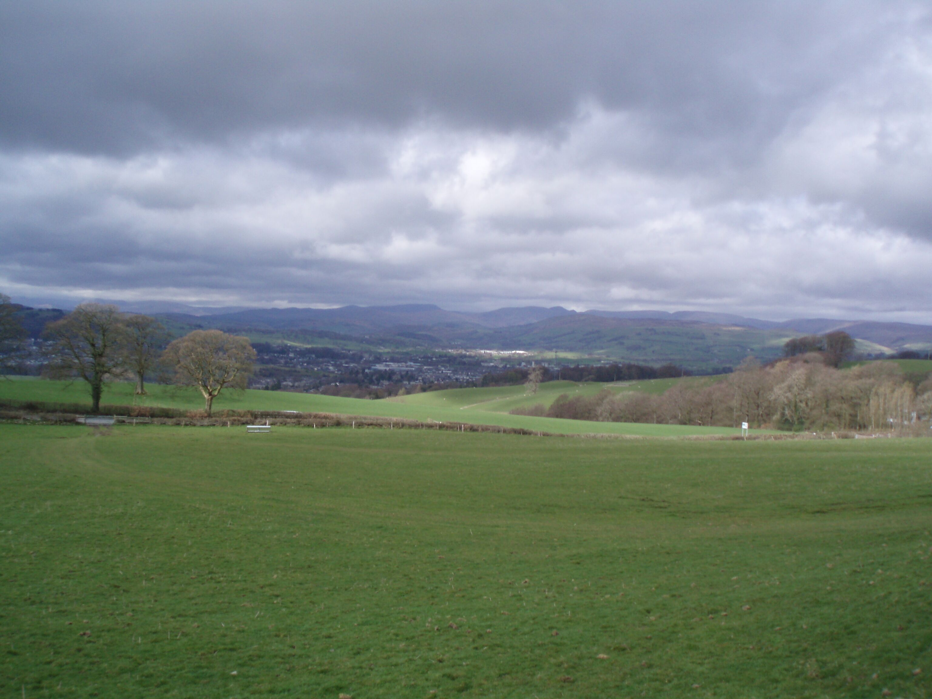 A rural landscape with rolling hills, a few scattered trees, and a distant town.
