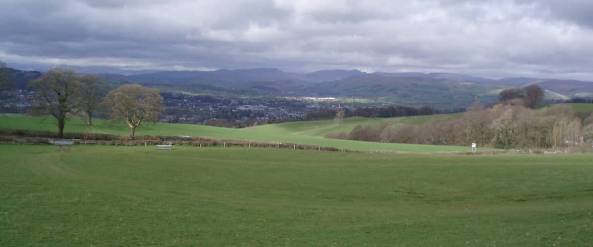 A rural landscape with rolling hills, a few scattered trees, and a distant town.