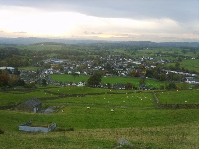 A rural landscape with a village, green fields, and sheep grazing.