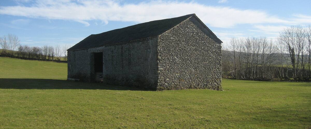 A stone building with a sloped roof in a grassy field.