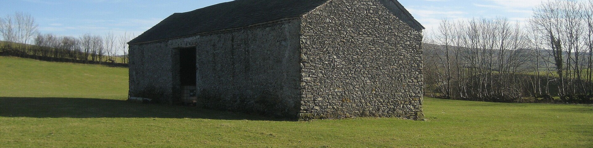 A stone building with a sloped roof in a grassy field.