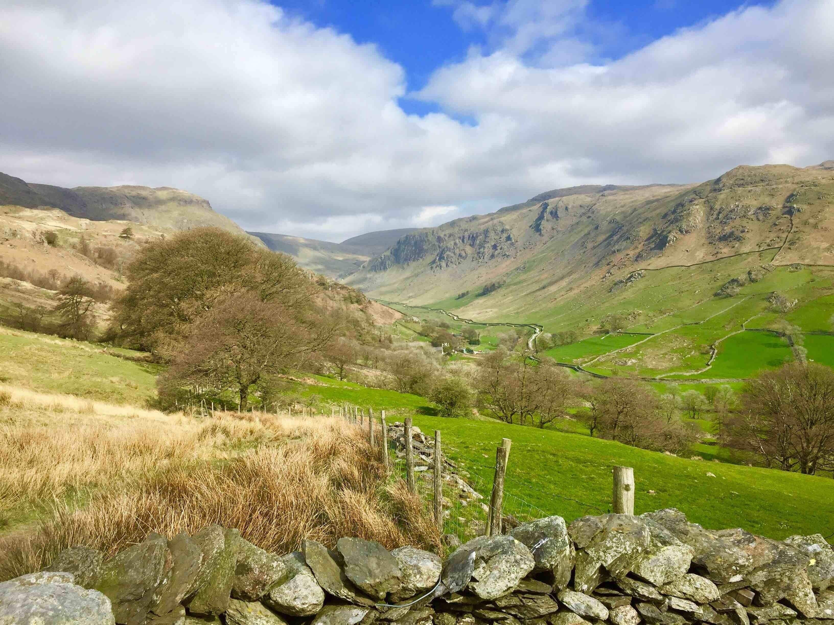 A valley with green fields, a stone wall, and mountains in the background.