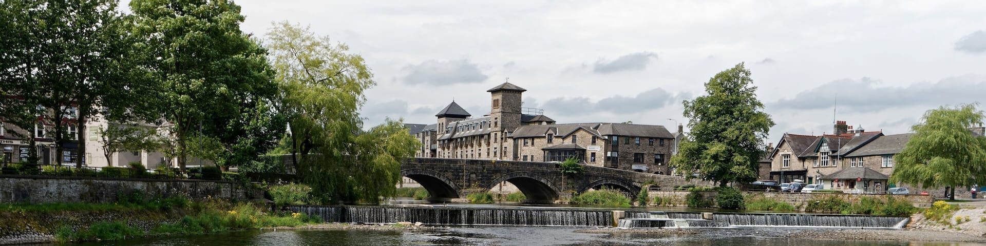 A river with a stone bridge, lush greenery, and a historic building in the background.