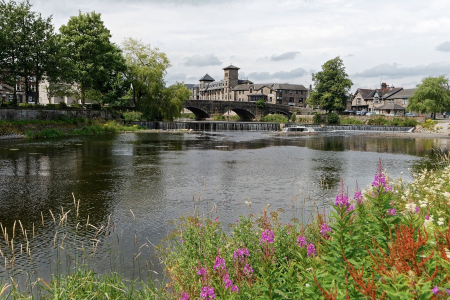 A river with a stone bridge, lush greenery, and a historic building in the background.