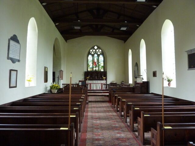 A church interior with wooden pews, a central aisle, stained glass windows, and a pulpit.