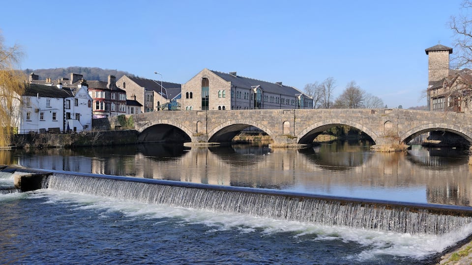 A stone bridge over a river with buildings and a tower on the right.