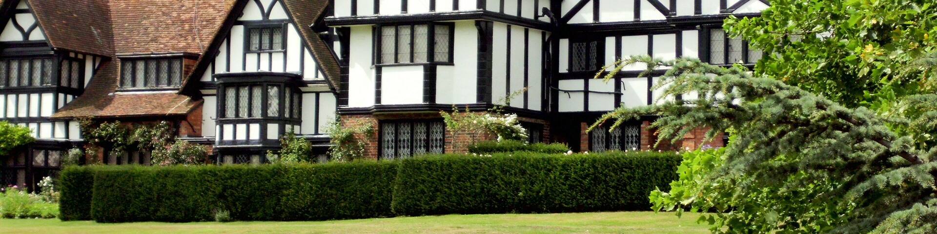 A row of Tudor-style houses with white and black timber framing, set in a lush green landscape.