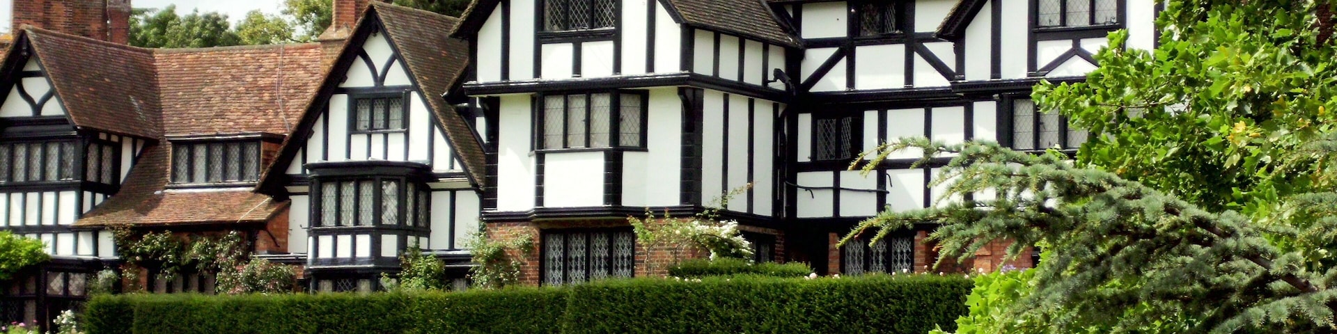 A row of Tudor-style houses with white and black timber framing, set in a lush green landscape.