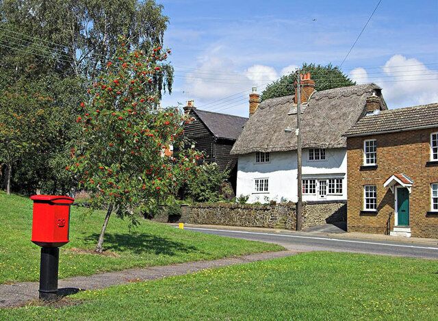 A rural street with traditional houses, a red post box, and a tree with red flowers.