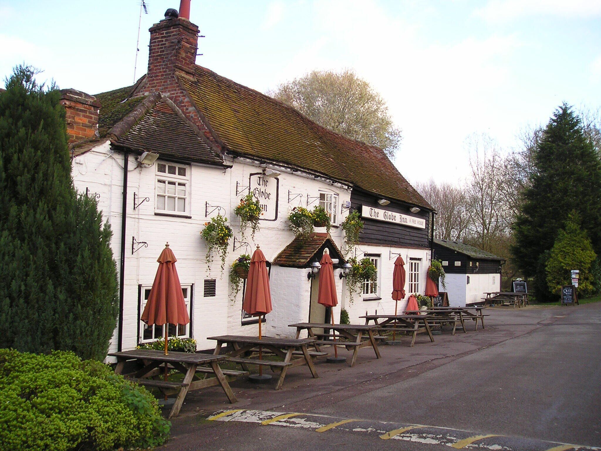A white building with a sign reading "The Globe Inn A Free House." There are wooden picnic tables and red umbrellas outside.