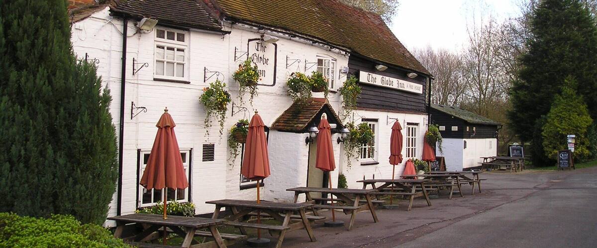 A white building with a sign reading "The Globe Inn A Free House." There are wooden picnic tables and red umbrellas outside.