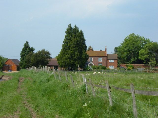 A rural landscape with a large house, a wooden fence, and a grassy field.