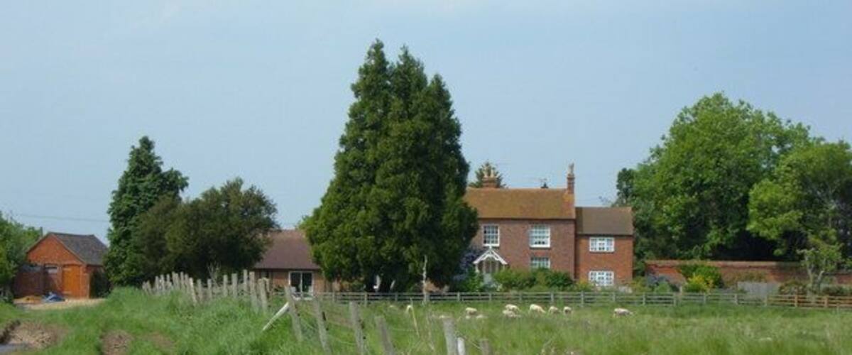 A rural landscape with a large house, a wooden fence, and a grassy field.