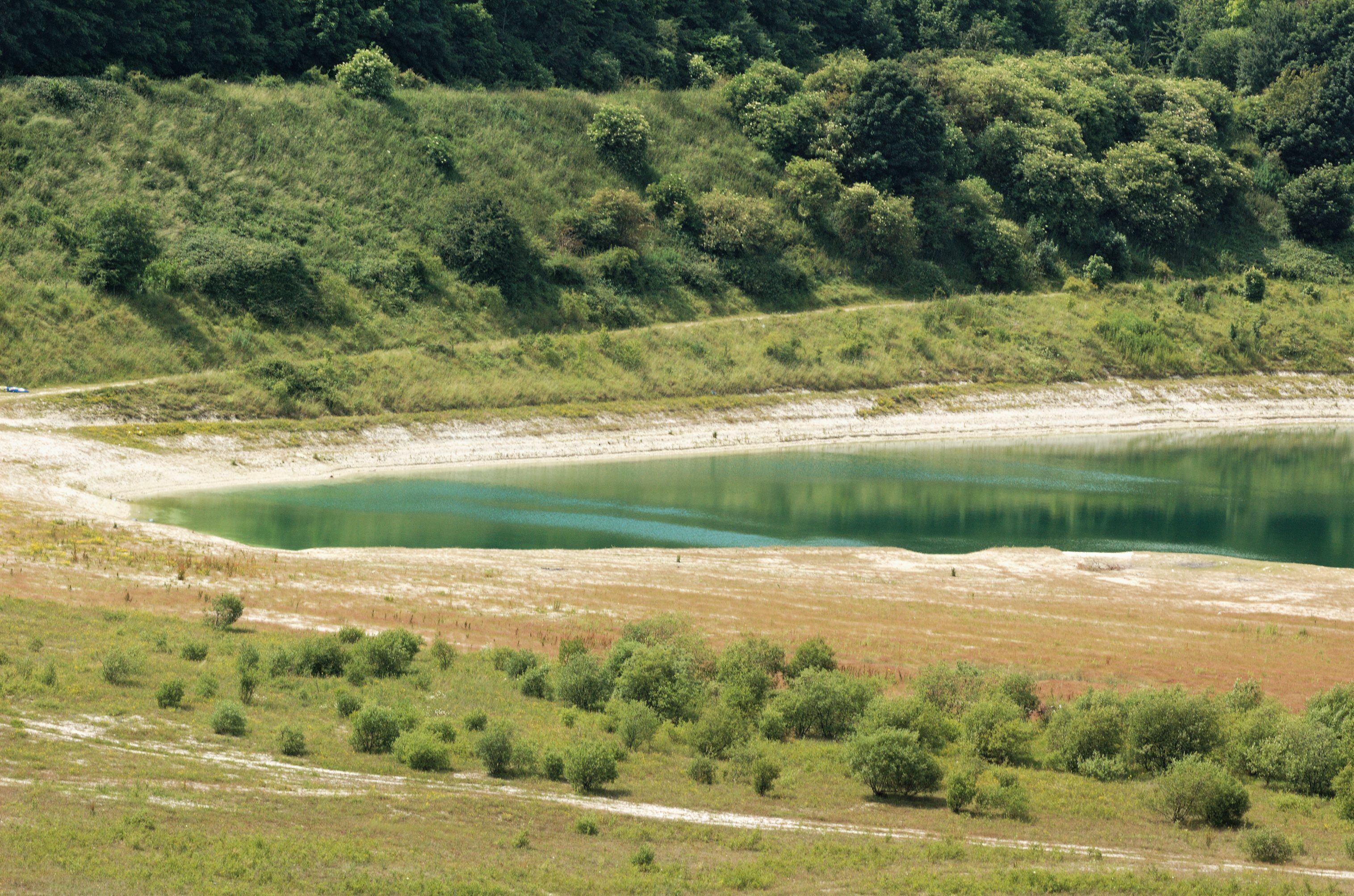 A lake surrounded by green hills and sparse vegetation.