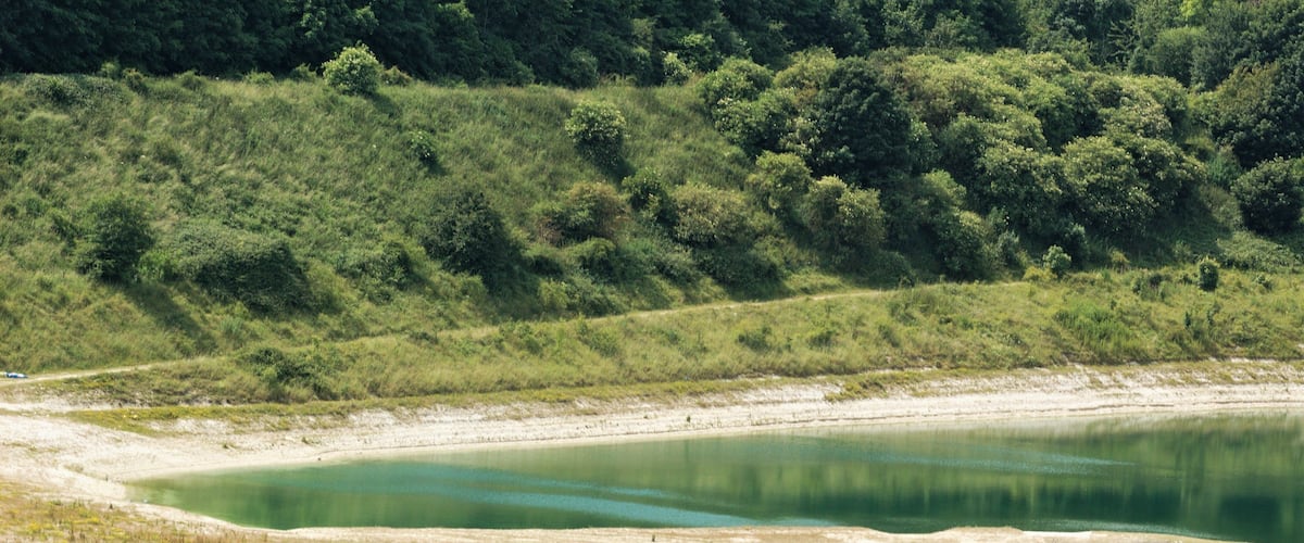 A lake surrounded by green hills and sparse vegetation.