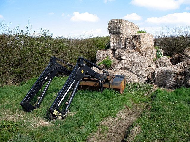 Loader and Bales A tractors front loader rests on the grass beside a pile of straw bales on Bury Farm.