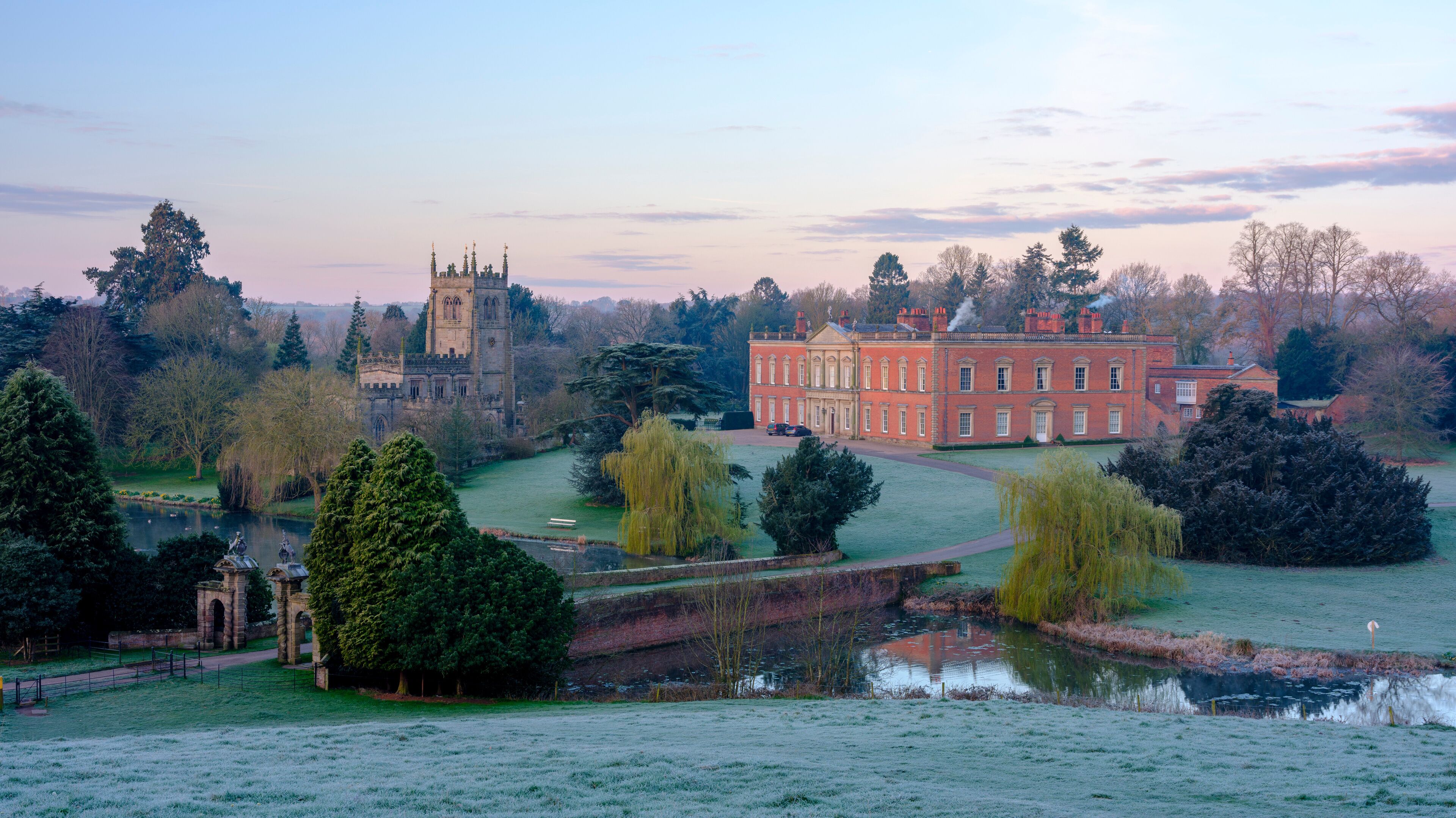 A historic building with a tower, a large pond, and surrounding trees.
