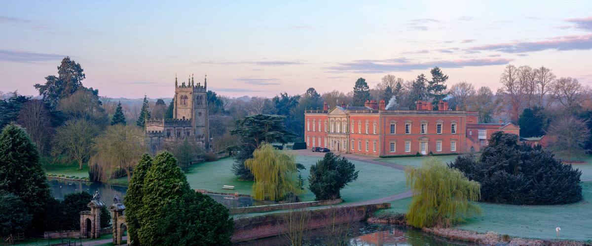 A historic building with a tower, a large pond, and surrounding trees.
