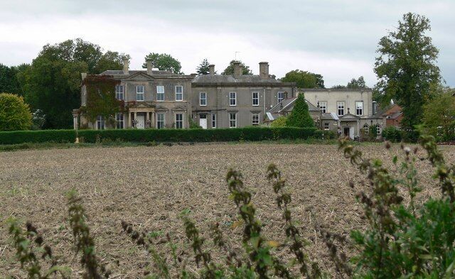 A large estate with multiple buildings, a well-maintained lawn, and a field in the foreground.