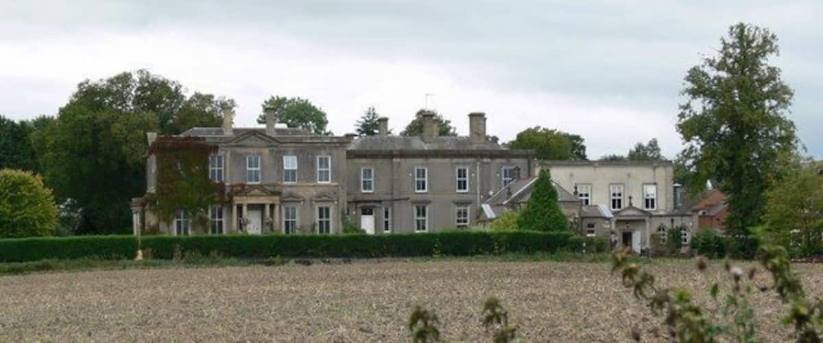 A large estate with multiple buildings, a well-maintained lawn, and a field in the foreground.