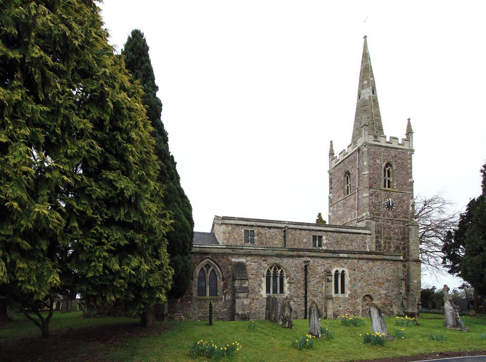 A historic church with a tall spire and a large tree in the foreground.