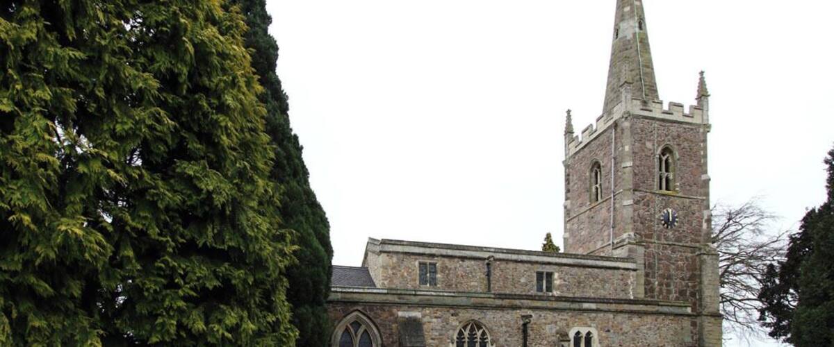 A historic church with a tall spire and a large tree in the foreground.