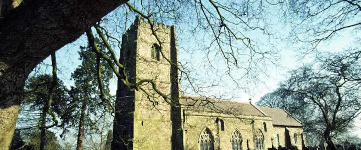 A church with a tall tower and arched windows, surrounded by a grassy field and trees.
