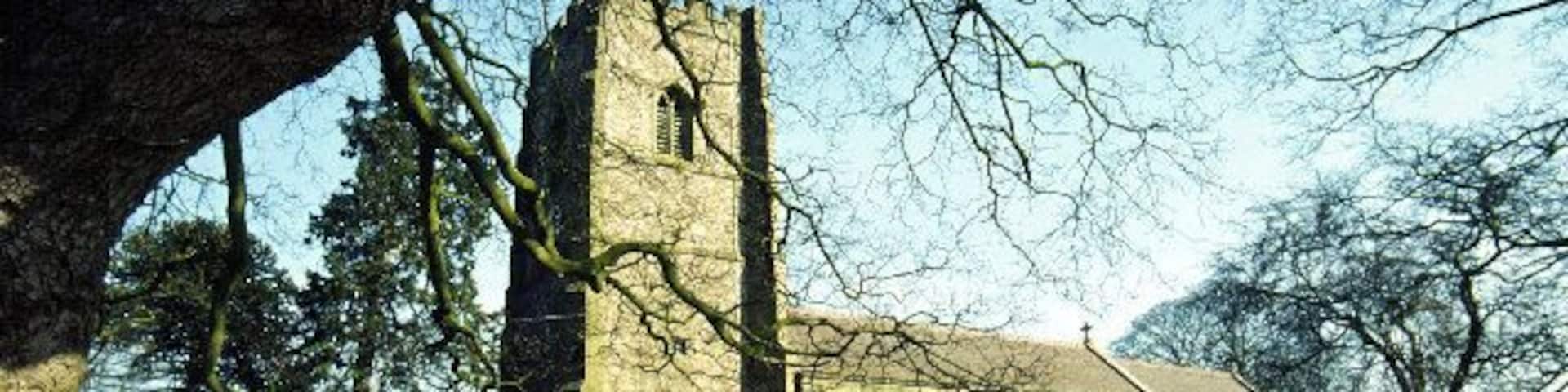 A church with a tall tower and arched windows, surrounded by a grassy field and trees.