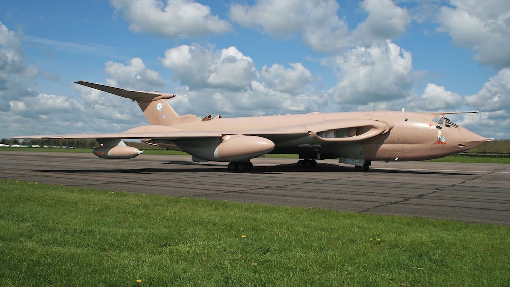 A military aircraft on a runway with a grassy area in the foreground and a partly cloudy sky in the background.