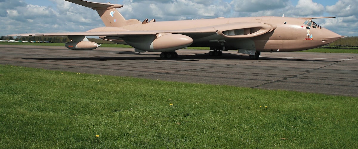 A military aircraft on a runway with a grassy area in the foreground and a partly cloudy sky in the background.