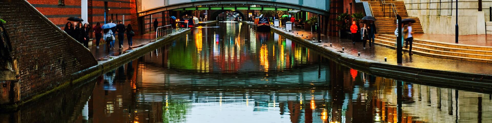 A canal with a bridge, red brick buildings, and a reflection of lights on the water.