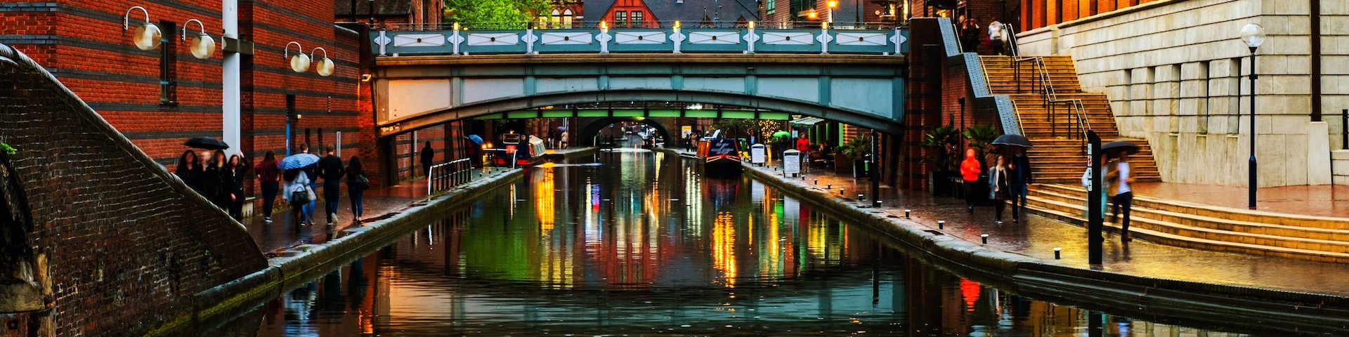 Um canal com uma ponte, edifícios de tijolos vermelhos e o reflexo de luzes na água.