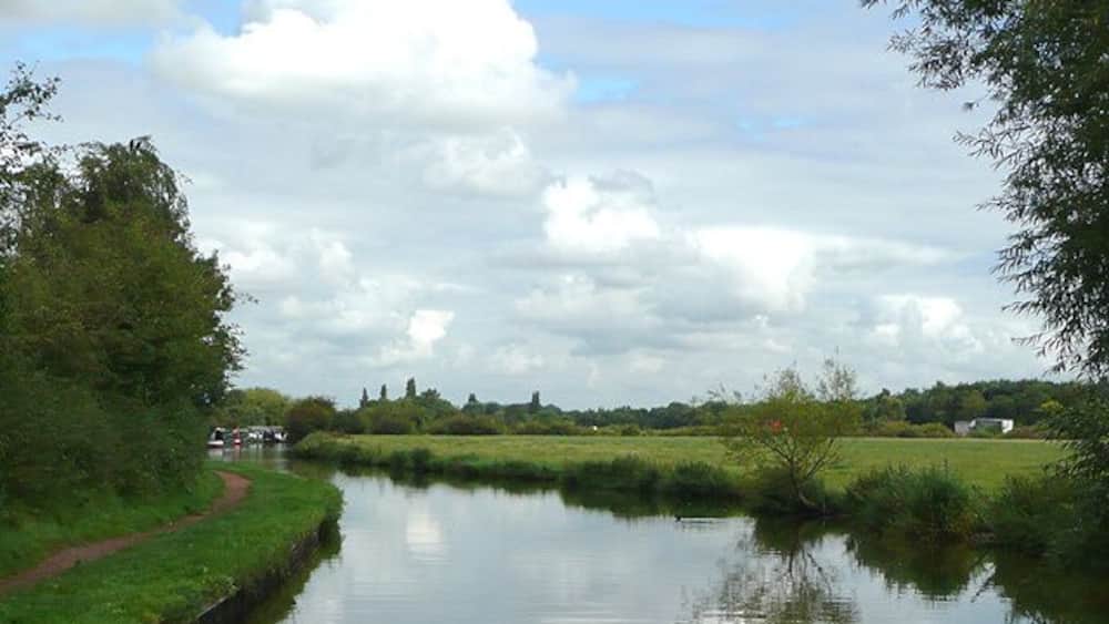 A calm river with a grassy bank, a path, and a distant white building.