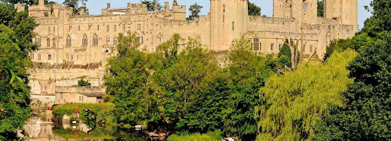 Um castelo histórico com fossado, cercado por vegetação exuberante e árvores.