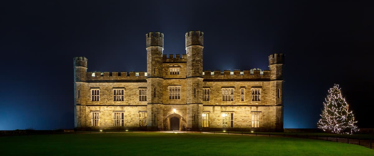 A large stone castle with multiple towers and a lit Christmas tree.