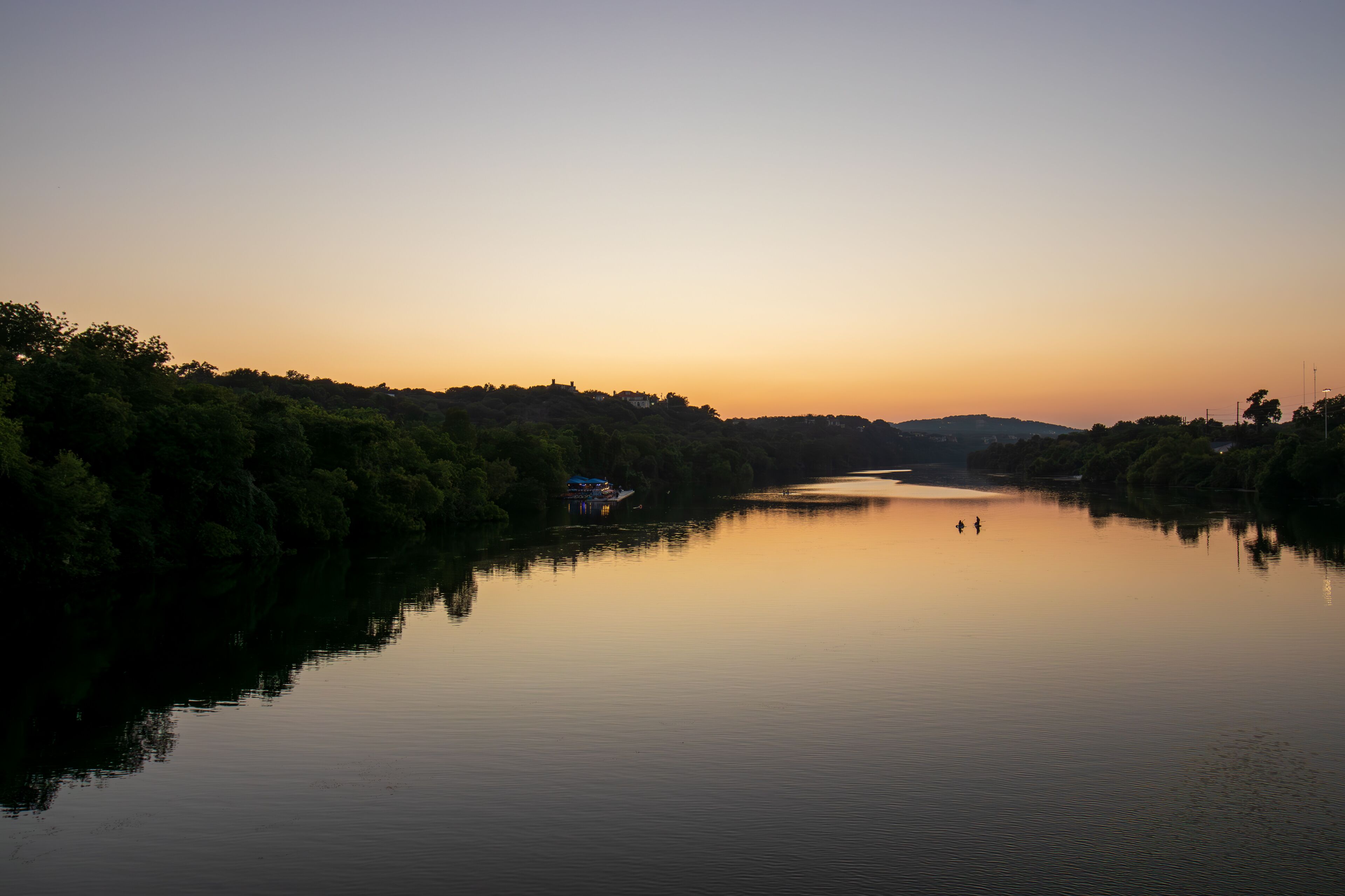 As the day gracefully transitions to dusk, Lady Bird Lake in Austin, Texas, becomes a canvas for nature's beauty. The serene river mirrors the warm tones of the setting sun.
