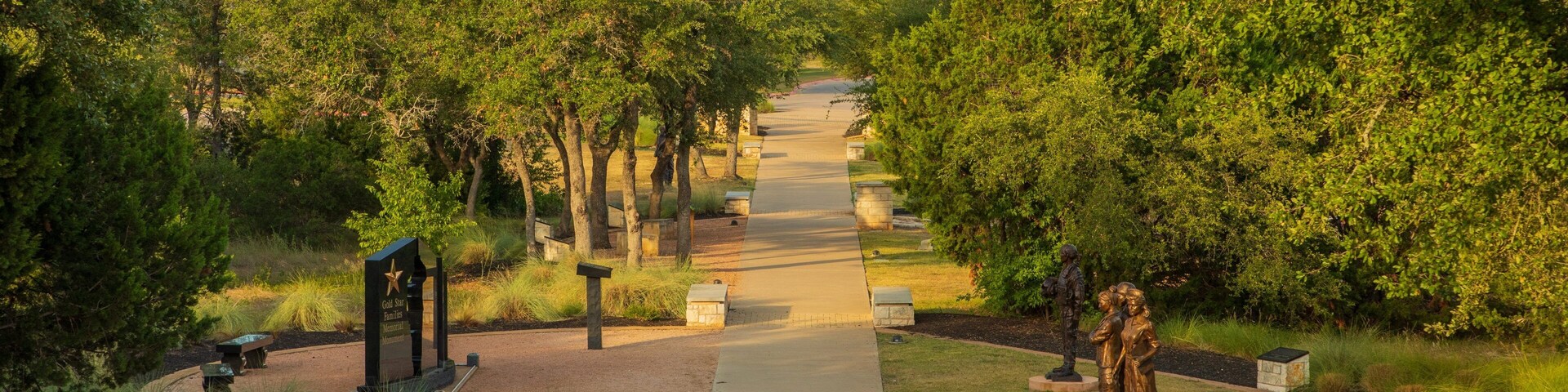 A memorial pathway flanked by trees and featuring a statue.