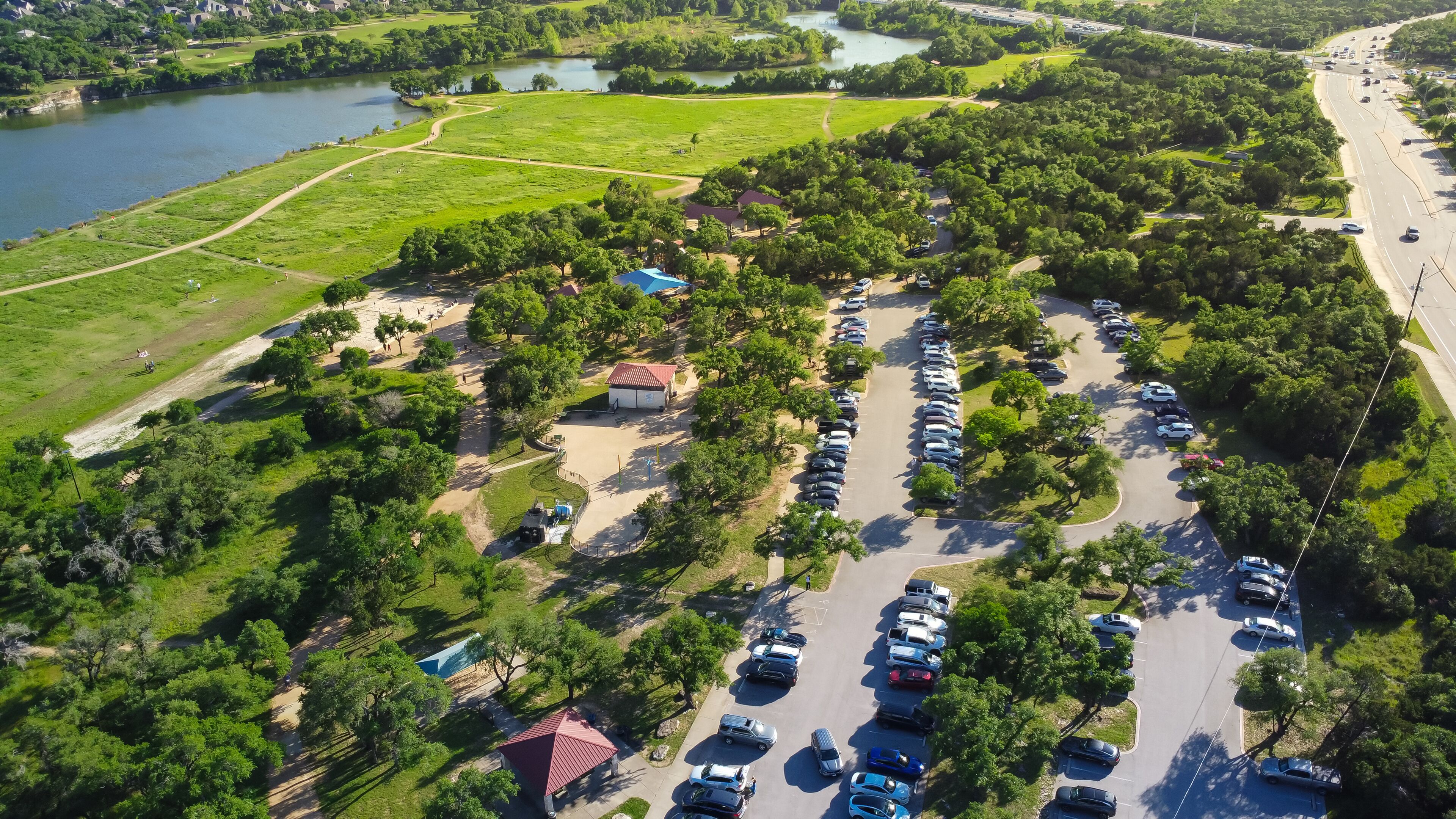 An aerial view of a parking lot surrounded by greenery and a body of water.