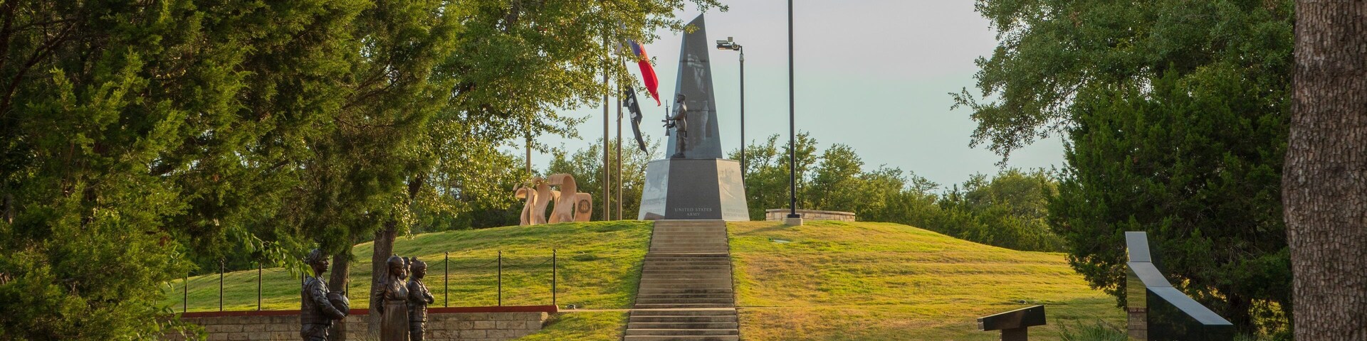Un monumento con una estatua, una bandera y un obelisco en una colina cubierta de césped.