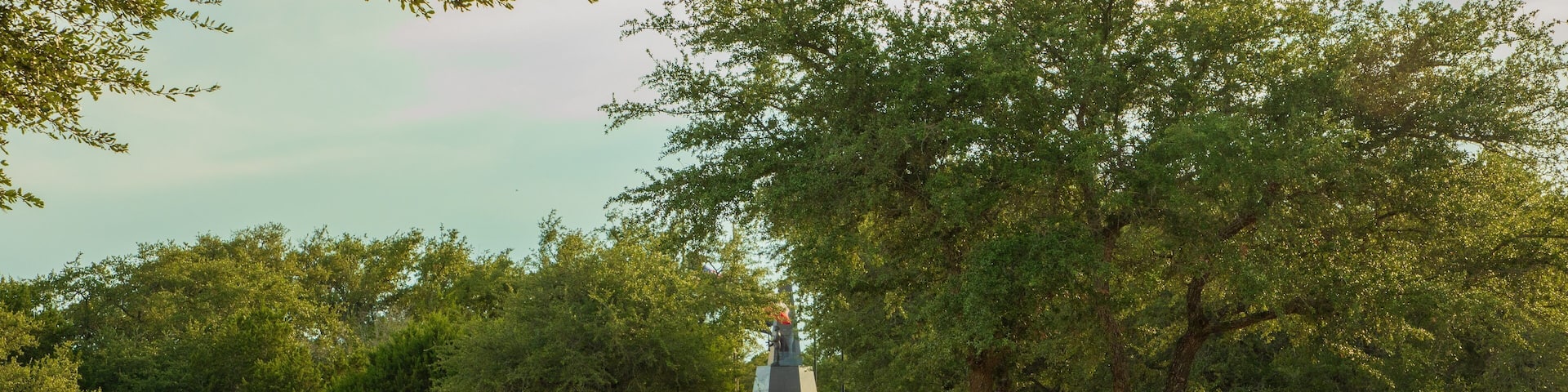 A memorial with statues and a central monument, surrounded by trees and a pathway.