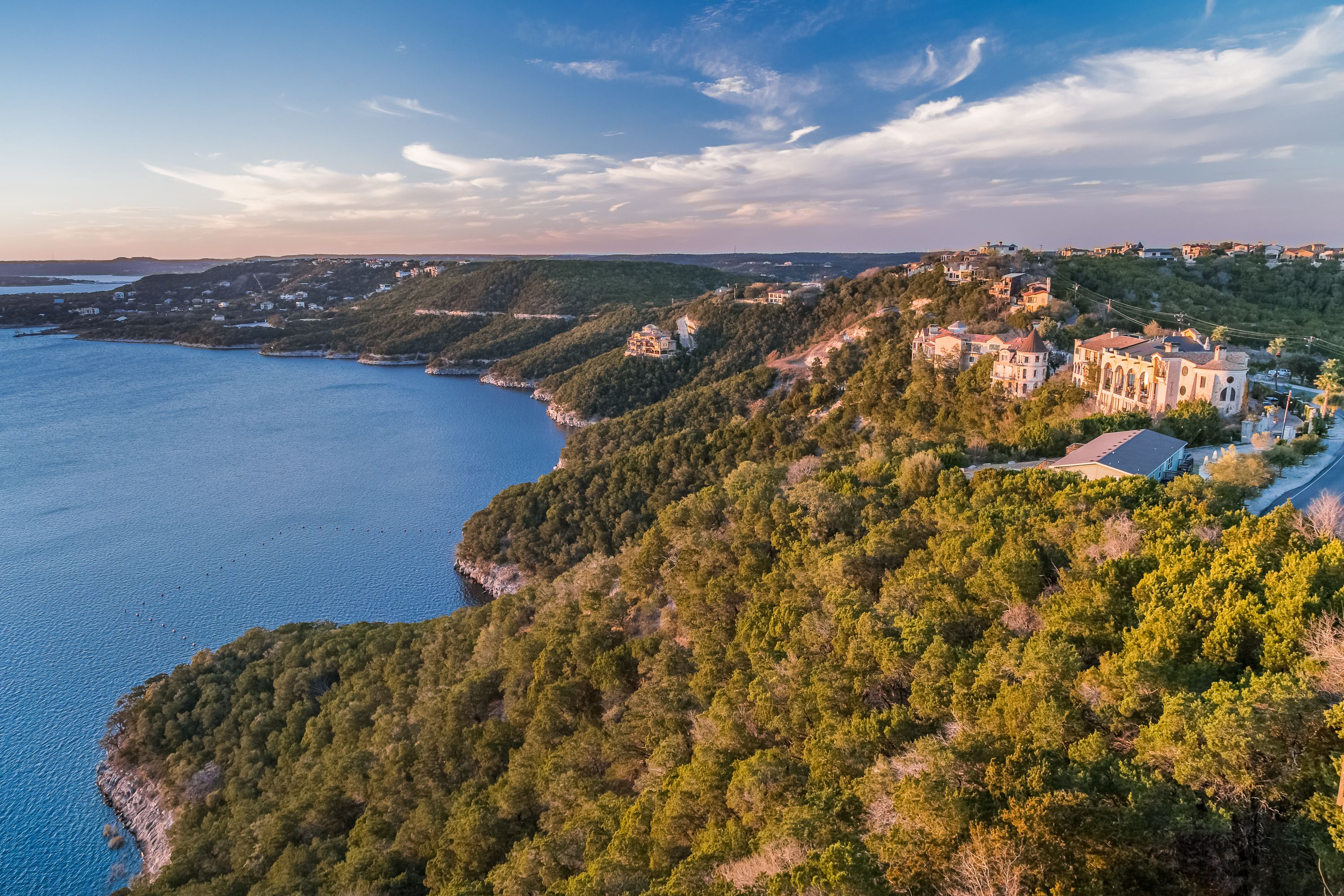 A coastal landscape with a clear sky, a body of water, and a hillside with buildings.