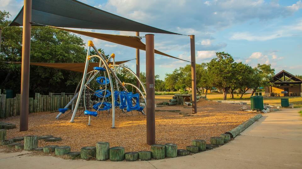 Un parque infantil con columpios y tobogán, rodeado de árboles y una zona de picnic.