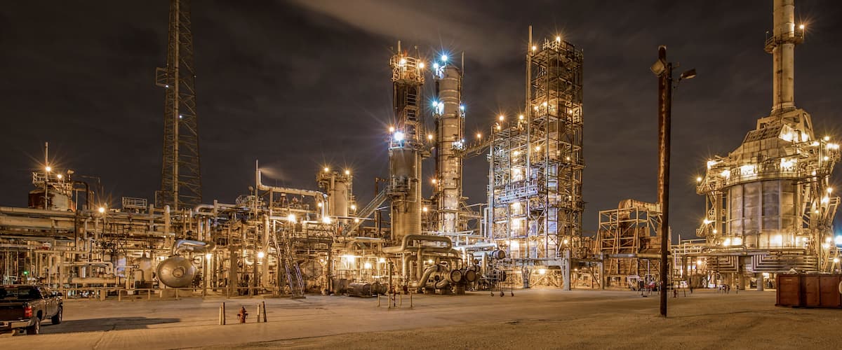 An industrial complex with multiple tall structures and extensive piping at night.