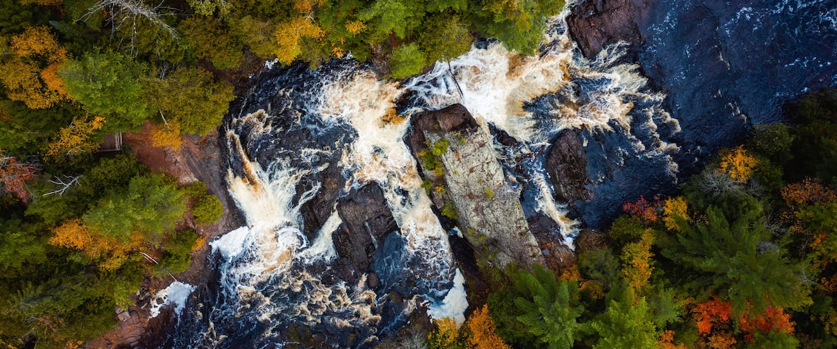 A river flowing through a forest with autumn-colored trees and rocky terrain.