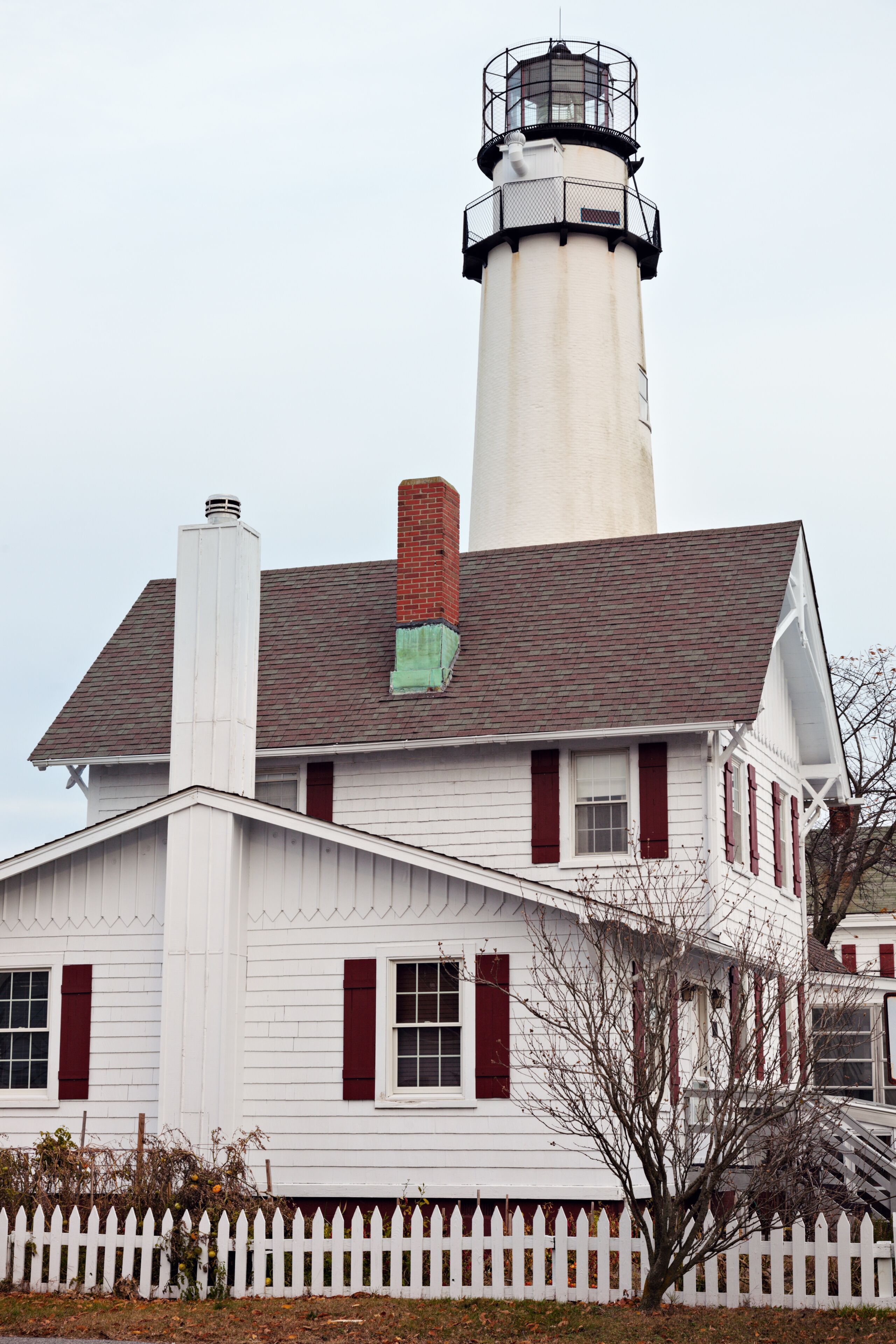 Un edificio blanco con contraventanas rojas y un faro al fondo.