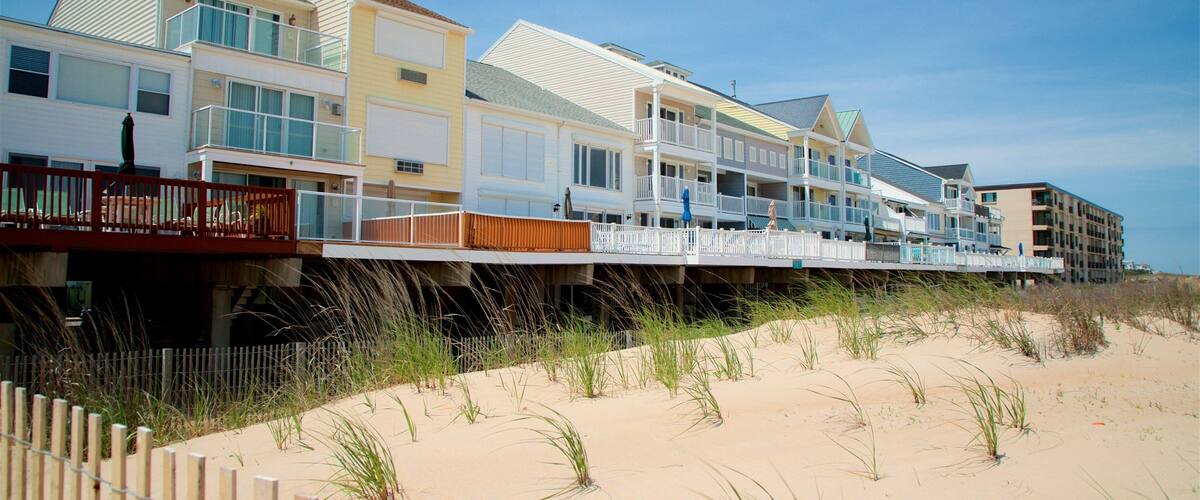 A beachfront residential area with multi-story houses, a wooden fence, and sand dunes.