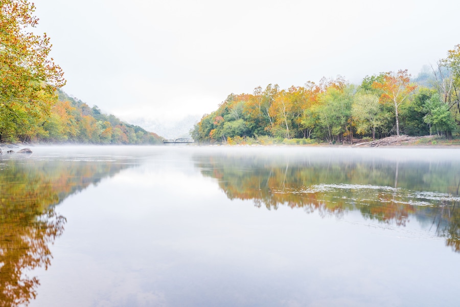 New River Gorge wide canyon water river lake during autumn golden orange foliage in fall by Grandview with peaceful calm tranquil morning bright mist fog